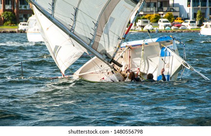 A girl and boy in the water climbing back into a capsized racing sailboat. Teamwork by junior sailors racing on saltwater Lake Macquarie. Photo for commercial use. - Shutterstock ID 1480556798