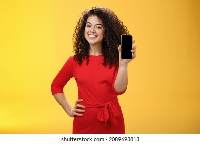 Girl brag with new phone she got on christmas feeling delighted holding mobile device in hand showing smartphone screena t camera, smiling broadly with uplifted mood over yellow background