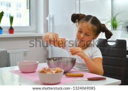 The girl breaks the egg. Little girl preparing cookies in kitchen at home. Cooking homemade food. Focus on girl's eyes.