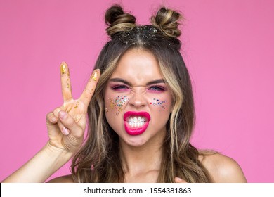 Girl with bright makeup grimaces on a pink background. Glitter Makeup.