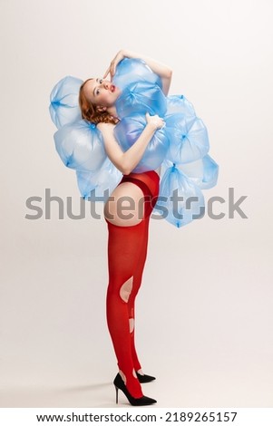Girl with bright makeup in red torn tights posing with plastic bags with water isolated over grey background. Weirdness. Concept of retro fashion, art photography, style, queer, beauty, youth