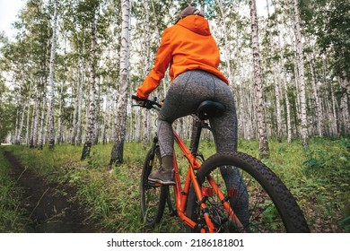 A Girl In A Bright Orange Jacket Riding A Red Bike Along A Path On Nature In Forest Close Up. Back View.