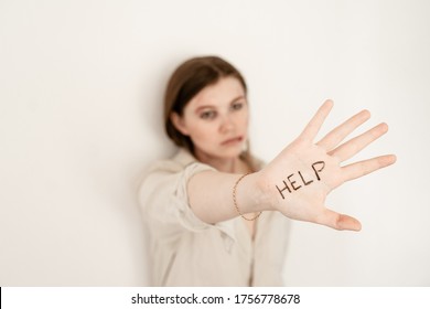 A Girl With Bruises From Domestic Violence Stands Against A White Wall, Pulled Out A Hand With The Inscription Help