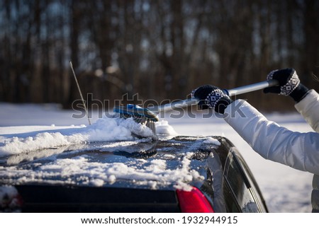 A girl with a brush in her hands cleans the roof of the car from snow. The car is covered with a large layer of snow. The car prepares for a trip after a heavy snowfall. Safety first
