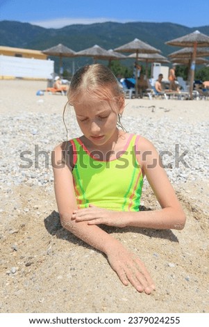 A girl is buried in the sand on the beach of the Adriatic Sea. Blonde girl in a yellow swimsuit.
