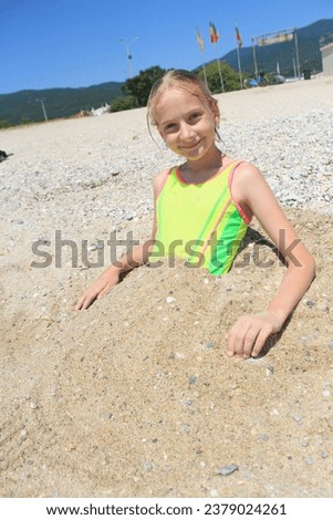A girl is buried in the sand on the beach of the Adriatic Sea. Blonde girl in a yellow swimsuit.