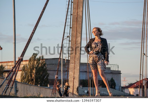 Girl in business style , on\
the bridge. On the phone. Go to work. Sunset, evening.\
Portrait.