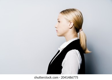 A Girl In A Business Suit With Her Hair Pulled Back In Profile Against A Gray Wall