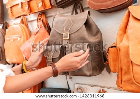 Girl buyer chooses a backpack on the market in the shop of leather Handicrafts