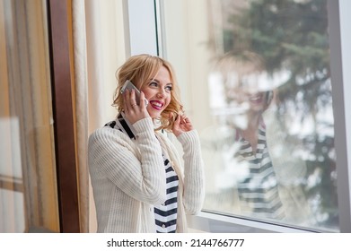 Girl Calling On Phone Land Line And Looking Outdoors Through A Window In The Living Room At Home.