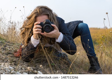 A Girl With A Camera In Her Hands In A Funny Pose Makes A Frame. Paparazi With A Camera In His Hands On An Outbreak In The Mountains.