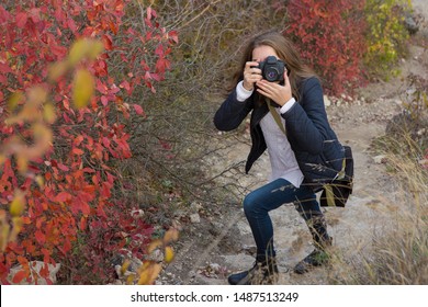 A Girl With A Camera In Her Hands In A Funny Pose Makes A Frame. Paparazi With A Camera In His Hands On An Outbreak In The Mountains.