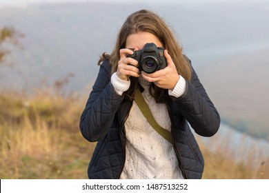 A Girl With A Camera In Her Hands In A Funny Pose Makes A Frame. Paparazi With A Camera In His Hands On An Outbreak In The Mountains.