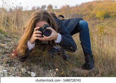 A Girl With A Camera In Her Hands In A Funny Pose Makes A Frame. Paparazi With A Camera In His Hands On An Outbreak In The Mountains.