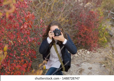 A Girl With A Camera In Her Hands In A Funny Pose Makes A Frame. Paparazi With A Camera In His Hands On An Outbreak In The Mountains.