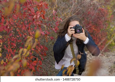 A Girl With A Camera In Her Hands In A Funny Pose Makes A Frame. Paparazi With A Camera In His Hands On An Outbreak In The Mountains.