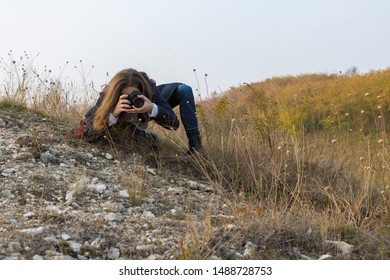 A Girl With A Camera In Her Hands In A Funny Pose Makes A Frame. Paparazi With A Camera In His Hands On An Outbreak In The Mountains.