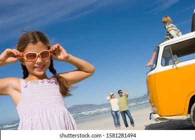 Girl at camera in sunglasses by camper van on family beach vacation - Powered by Shutterstock