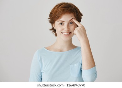 Girl Can Not Lift Her Eyebrow Without Help Of Hand. Portrait Of Happy Attractive Redhead Female Student With Freckles In Ordinary Clothes Pulling Brow With Index Finger, Smiling And Being In Good Mood