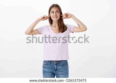 Girl cannot do homework in such noise. Displeased intense bothered female with tattoo clenching teeth closing ears with index finger looking at upper right corner interrupted with loud sound