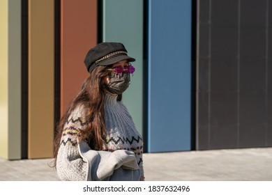 A Girl In A Cap And Pink Glasses Stands On The Street With A Black Protective Mask On Her Face. See Through Rose-tinted Glasses