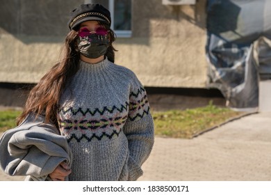 A Girl In A Cap And Pink Glasses Stands On The Street With A Black Protective Mask On Her Face. See Through Rose-tinted Glasses