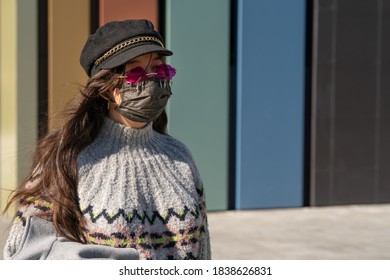 A Girl In A Cap And Pink Glasses Stands On The Street With A Black Protective Mask On Her Face. See Through Rose-tinted Glasses