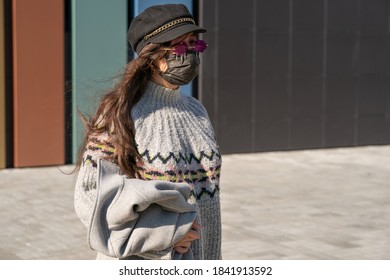 A Girl In A Cap And Pink Glasses Stands On The Street With A Black Protective Mask On Her Face. See Through Rose-tinted Glasses