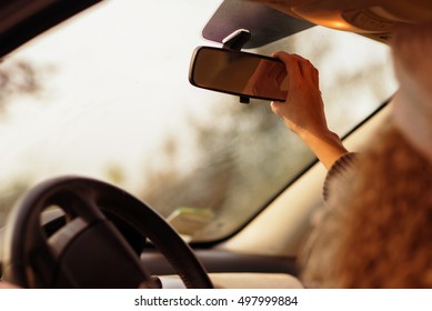 the girl in the car adjusts the rear view mirror