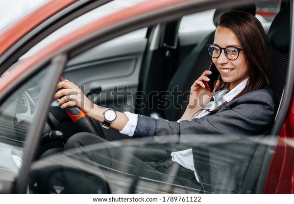 The girl in the car behind the wheel looks at the\
notification phone and reads the message. A woman in a parking lot\
sits in a auto.