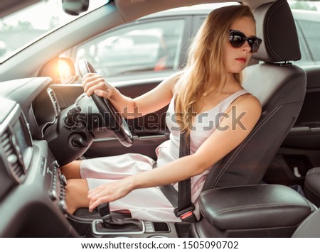girl car, right-hand drive, left-hand traffic, reversing, parking lot near shopping center. Engaging reverse gear, looking at rear window, checking back row passengers, driving safety at mall.