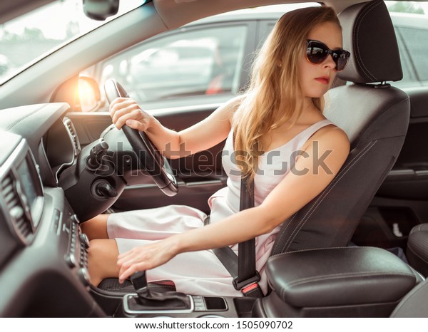 girl car, right-hand drive, left-hand traffic,
reversing, parking lot near shopping center. Engaging reverse gear,
looking at rear window, checking back row passengers, driving
safety at mall.