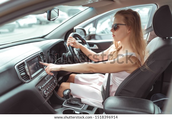 girl in\
car selects application on touch screen, navigation application on\
Internet, strapped holds wheel, left-hand traffic, wheel on right\
side. Woman in summer sunglasses in\
city