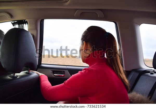 The girl in the car sits in the\
back seat. The girl is looking out the window. Back view,\
back.