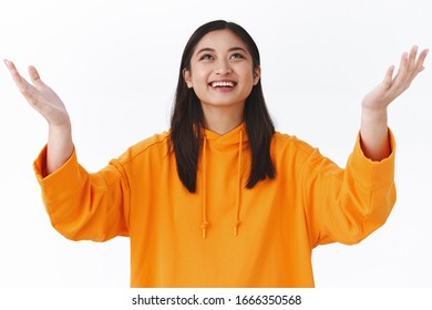 Girl Catching Something From Sky. Cheerful Happy Asian Woman Raising Hands Up And Smiling Looking Upwards At Falling Object, Thanking God, Feel Relieved And Delighted Dream Come True, Accomplish Goal