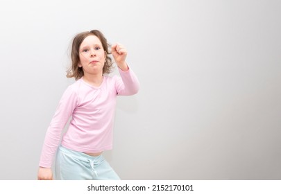 Girl, Caucasian 6 Years Old, In A Pink Coat On A Gray Background. The Child Is Happy And Smiling, Waving His Arms And Dancing