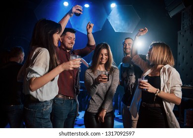 Girl Is In The Center Of Attention. Happy People Dancing In The Luxury Night Club Together With Different Drinks In Their Hands.