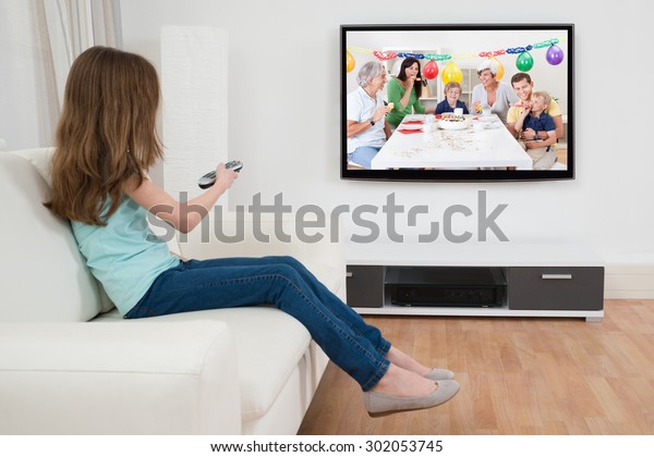 自宅でテレビの前でリモコンでチャンネルを変える女の子 の写真素材 今すぐ編集
