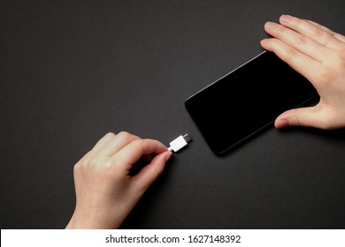 The girl charges a smartphone on a black background. View from above. Flatlay. Phone charging. Close up Mobile phone Charger with USB Type-C (USB-C). USB type C cable charger and port of the phone. 