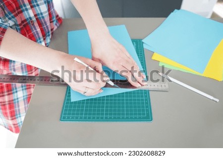 A girl in a checkered shirt cuts colored paper with a knife on a mock
