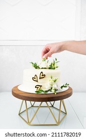 Girl Chef Decorates Wedding Cake With Flowers. White Wedding Cake With Floral Decoration On Wooden Stand. 