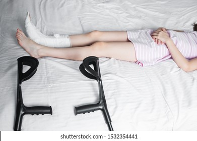 Girl child with a broken leg in a cast lies on a bed with crutches - Shutterstock ID 1532354441