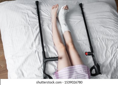 Girl Child With A Broken Leg In A Cast Lies On A Bed With Crutches