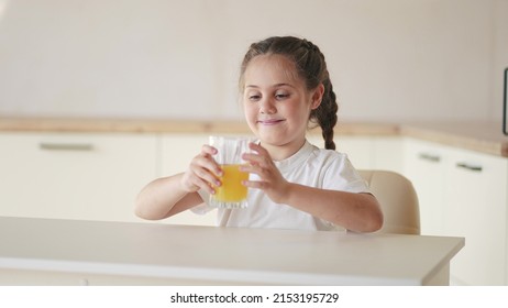 Girl Child Drinking Juice. Happy Family A Healthy Eating Kid Dream Concept. Daughter Girl Drinking Indoors Yellow Juice From A Glass Cup In The Kitchen. Child Drinking Fruit Juice