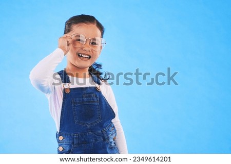 Girl child, glasses and frame in studio portrait for vision, health and eye care by blue background. Female kid, test spectacles and young fashion model with lens, smile or eyesight with mockup space