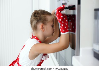 Girl Child In Gloves Waiting For Baking Muffins Or Cupcakes Near Oven.The Little Girl Looking At Tasty Fruitcake In The Oven. Cooking Process On Kitchen