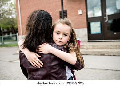 A girl child and his mother hugging outside at school