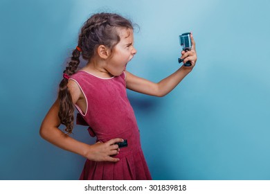 Girl child holding a camera in his hand shooter opened her mouth  shouts gray  background