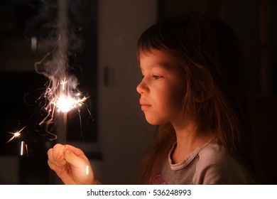 Girl, Child Holds In His Hands A Sparkler On A Dark Background At Home