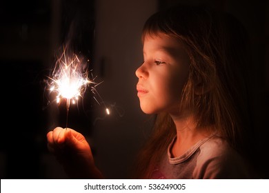 Girl, Child Holds In His Hands A Sparkler On A Dark Background At Home